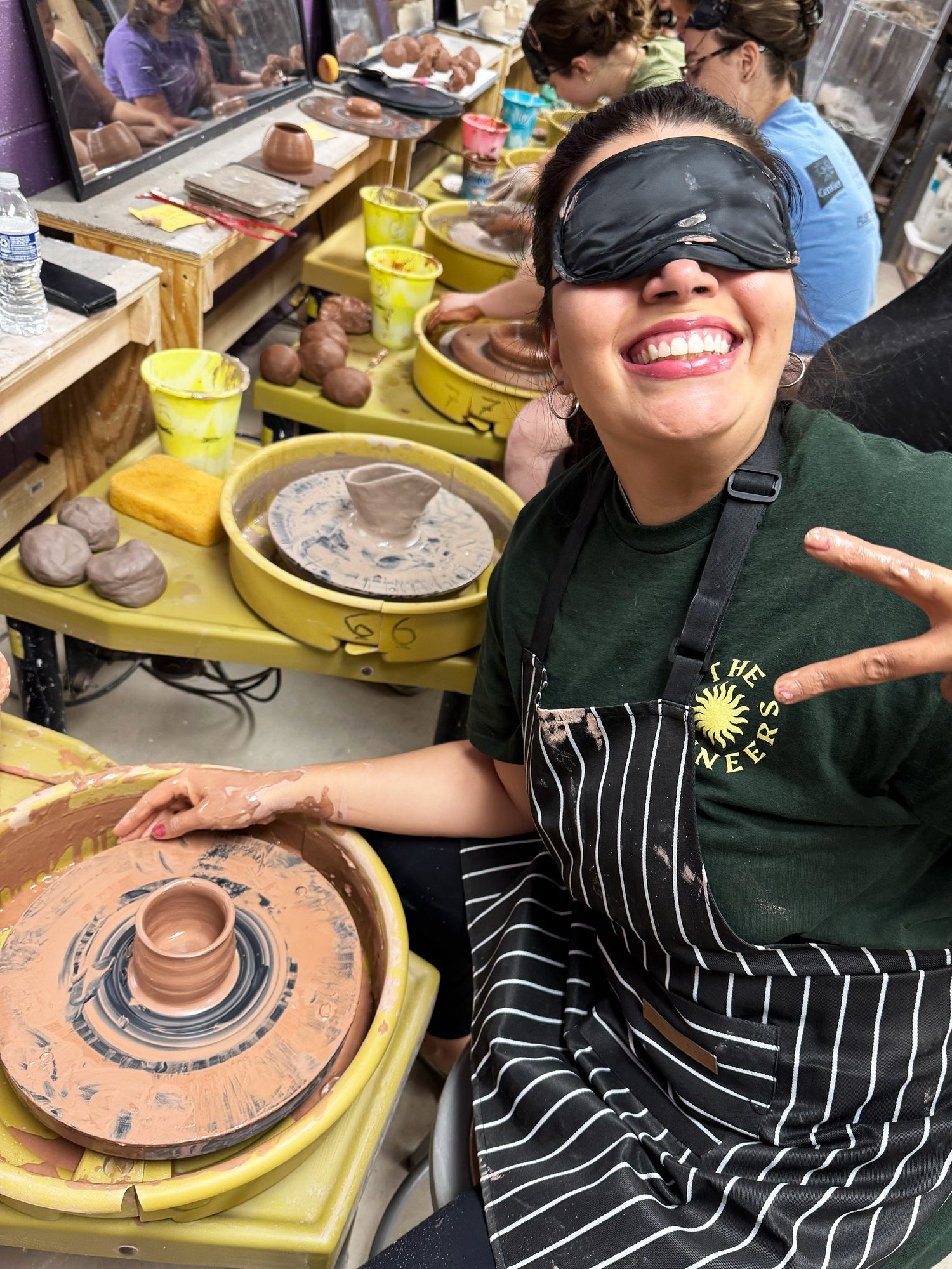 Person wearing a sleep mask in a pottery studio with clay pots and tools around